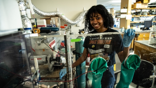 Young black woman wearing blue latx gloves working in a Biomeidcal Engineering lab.