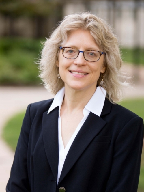 head shot of blonde woman with shoulder length hair and eyeglasses wearing a black suit jacket and white blouse with a collar