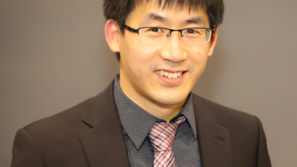 Man with short dark hair and glasses wearing dark blazer with tie