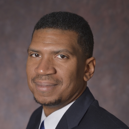 head shot of black male with black short hair wearing a dark grey suit with a shite shirt and a blue tie