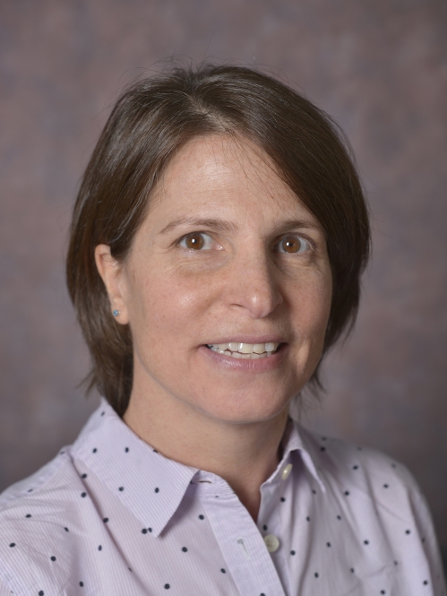 head shot of female with short brown hair wearing a light pink button down shirt with black polka dots