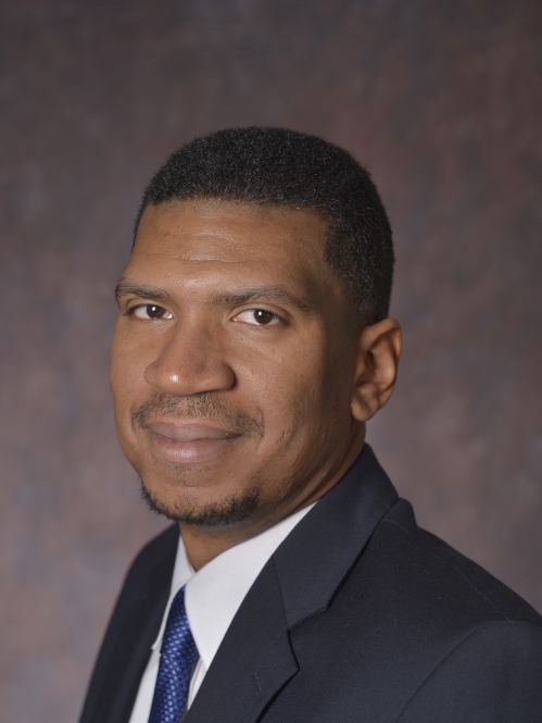 head shot of black male with black short hair wearing a dark grey suit with a shite shirt and a blue tie