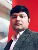 Headshot of Indian male with short, black hair, wearing a grey suit jacket with a pink button down shirt.