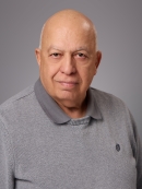 Headshot of bald male wearing a grey polo shirt underneath a grey pullover sweater.