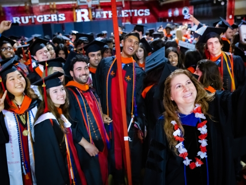 group of students in regalia at graduation taking a selfie with female professor