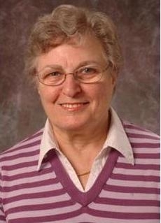 head shot of woman with short curly hair with eyeglasses wearing a striped pink and purple sweater with a collared shirt