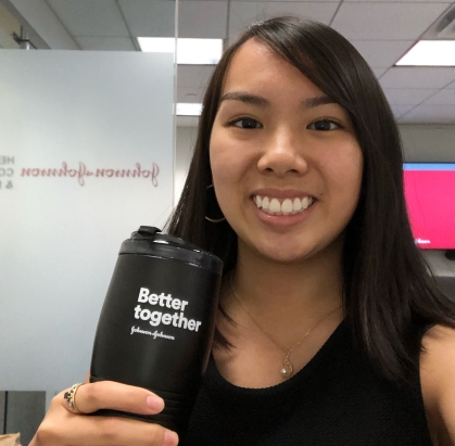 Headshot of young woman with long, black hair holding a Johnson and Johnson black travel mug that says "Better  together".