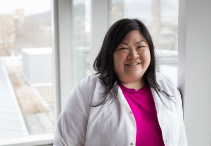 Headshot of a female with black, straight hair wearing a white lab coat over a pink shirt.