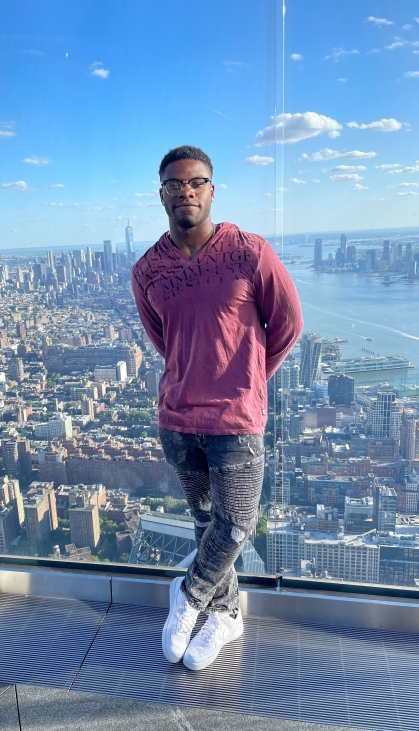 Black male with eyeglasses standing in the foreground of a cityscape.
