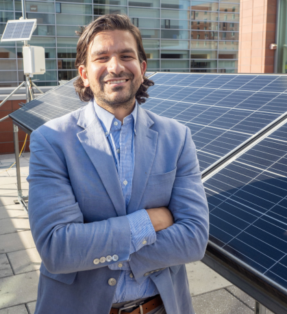 Man with facial hair and folded arms on rooftop with solar panels