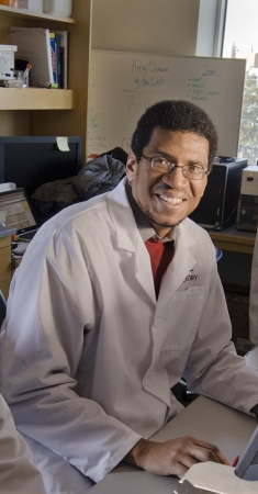 black man sitting in a laboratory wearing eyeglasses and a white lab coat