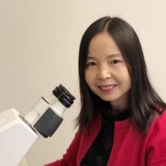 head shot of Asian woman with long black hair sitting next to microscope wearing a red blazer with a black shirt