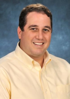 Headshot of white male with short brown hair wearing a yellow button down shirt.