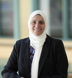 Woman wearing a white headscarf and a balck jacket.